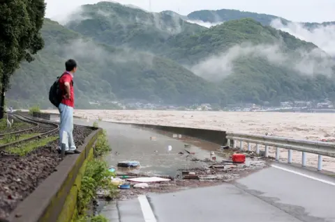 AFP A man looks at the overflowing Kuma river in Yatsushiro, Kumamoto prefecture, 4 July