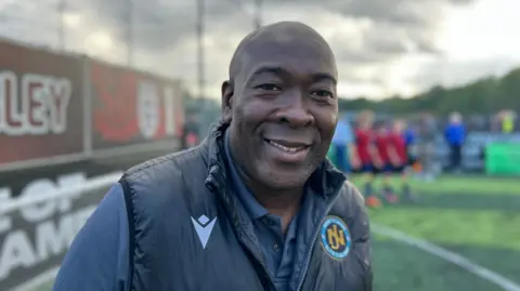 Man smiles at camera, he is wearing a dark jacket and shirt