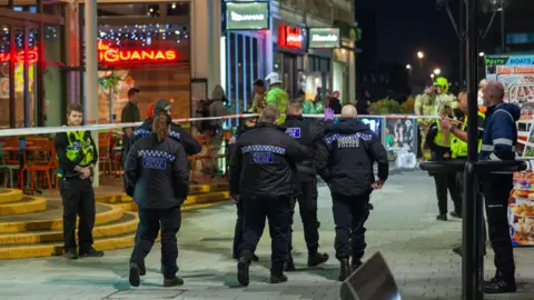 Beyond The Lens Photography Police officers near Las Iguanas restaurant in Cardiff Bay after the incident, with police tape stretched across the pavement and firefighters in the background