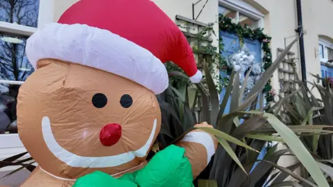 A inflatable gingerbread man outside a house with a white wreath and blue door.