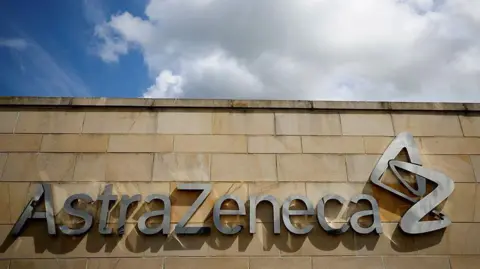 Reuters A sign on a building in silver saying AstraZeneca. It is on a sandstone brick wall and above it there is a blue sky with white clouds.