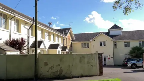 Exterior view of Oakmore Lodge, with the two-storey buildings alongside a car park, behind a wall