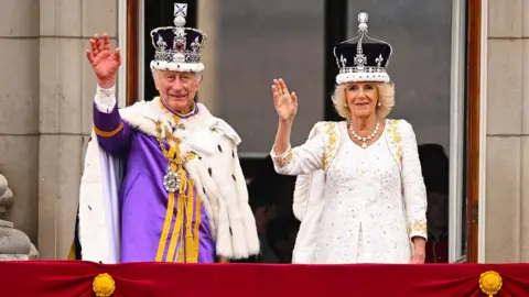 King Charles and Queen Camilla on the Buckingham Palace balcony wearing crowns and robes