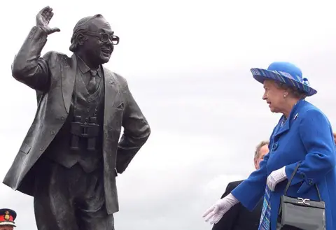 Getty Images Queen Elizabeth II, dressed in blue coat and hat, is standing near a statue of Eric Morecambe