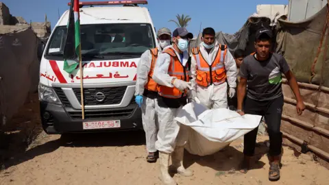 Workers carry bodies of unidentified Palestinians in body bags in Gaza. An ambulance is behind them. 