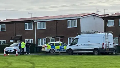 The outside of a property off Ostend Road in Walcott. There is a police car parked outside and a police officer is stood within the shot.