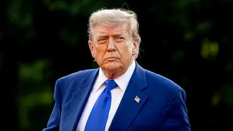Donald Trump scowls as he walks, wearing a blue suit and tie, on 24 June 2025