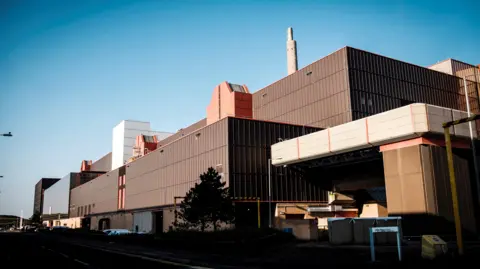 NDA A general view of the Thorp reprocessing plant. It is a large industrial-looking building with sections of different height and is covered in brown panelled cladding.