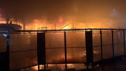 Mid and West Wales Fire Service Fire behind a fence at Tata Steel plant.