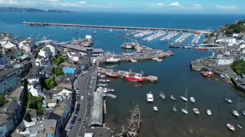 An aerial shot of a harbour with a large number of boats in a marina and a town on the left with roads and houses.