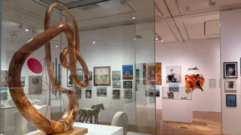 An art gallery displaying multiple pieces of art, including a wooden sculpture and canvas hanging on the wall.