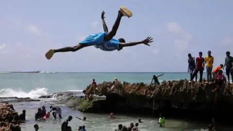 Feisal Omar/Reuters A man jumps into the Indian Ocean waters to join others in Somalia, Mogadishu on 7 June. 