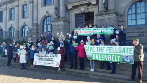 Protesters standing outside South Shields Town Hall. About 40 people are standing on the steps of the town hall and are holding signs reading, Save The Fields and Save The Fellgate Greenbelt.