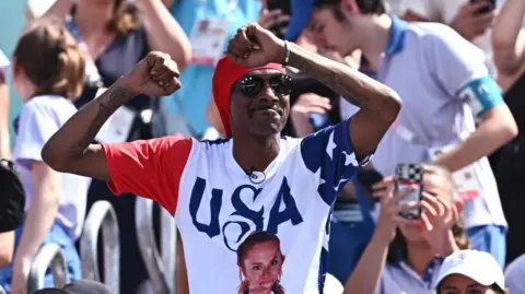 Reuters De Amerikaanse rapper Snoop Dogg in een T-shirt met een foto van Kelly Cheng wordt vóór de wedstrijd op de tribune zien dansen.