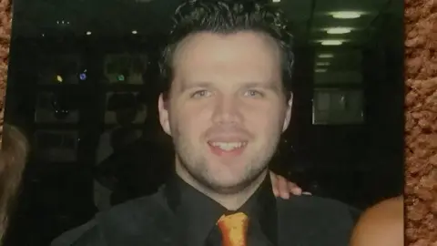 Family handout Paul Keany with short black hair wearing a black shirt and a gold tie