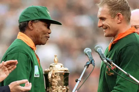 Getty Images South Africa's president Nelson Mandela congratulates South Africa's rugby team captain François Pienaar before handing him the William Webb trophy after his team's victory over New Zealand (15-12) in the final of the Rugby World Cup at Ellis Park in Johannesburg 24 June 1995