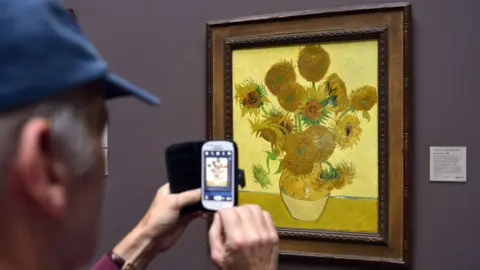 BBC Stock photo of a man taking a photo of Van Gogh's Sunflowers at the National Gallery