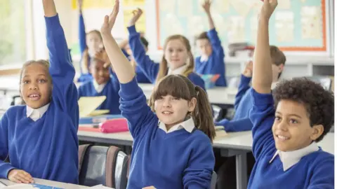 Caiaimage/Chris Ryan Elementary school children wearing blue school uniforms raising hands in classroom - stock photo