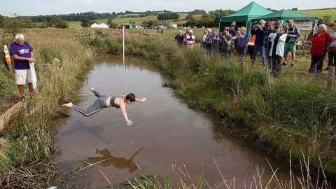 World Alternative Games Crowds watches as a woman jumps, arms and legs spread, into the water