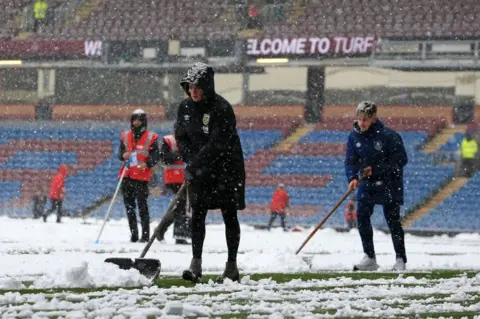 LINDSEY PARNABY/Getty Images Membersof the ground staff clear snow from the lines as the snow falls ahead of the English Premier League football match between Burnley and Tottenham Hotspur at Turf Moor in Burnley, north west England