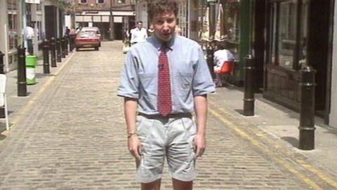 Rob Curling stands in a cobbled street wearing a shirt, tie and shorts.