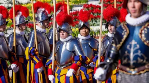 Reuters Swiss guards line up, wearing their traditional, colourful uniforms and helmets with red feather plumes