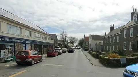 A view of the high street in St Martin showing a road with houses along either side and cars travelling down the road.