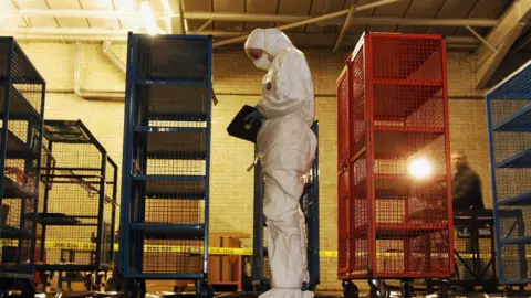  A police forensic officer, dressed white overalls, inspects money cages that were used to store banknotes, stolen from the Securitas Depot in Tonbridge.