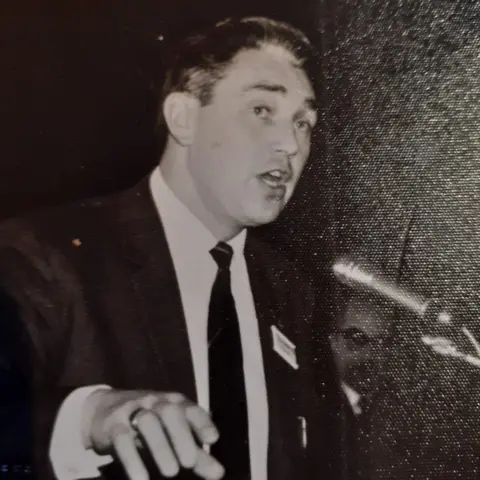 DAGCAS A black and white image of a man speaking into a microphone