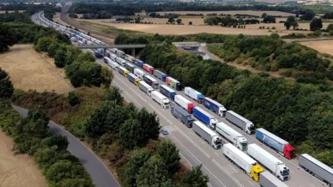 Hundreds of lorries on a motorway. They are queueing heading out of the frame.