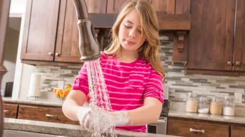 Getty Images Girl in pink top washes hands in kitchen sink