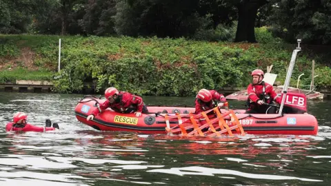 Four firefighters practice a water rescue on a boat. 