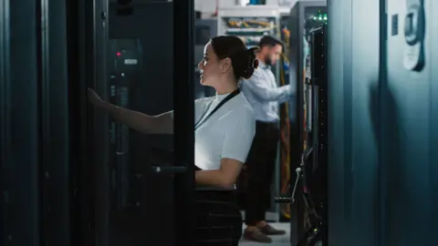 A woman and a man working in a server room.