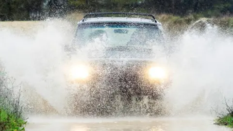 Getty Images A car drives through rain and puddles