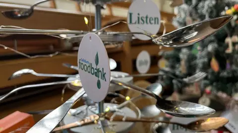 A foodbank bauble hanging from a spoon, which is acting a tree branch 