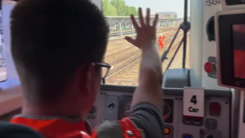Liam driving a train, waiving to an engineer on the track nearby