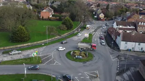 East Riding of Yorkshire Council A roundabout in Bridlington, with lots of roads stemming from it. A lorry with a red cabin at the front is going round and there is a white building on one corner. The roundabout has a green grass island in the middle.