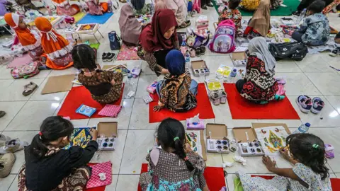 NurPhoto via Getty Images Little girls sitting on the floor painting, with teachers helping them