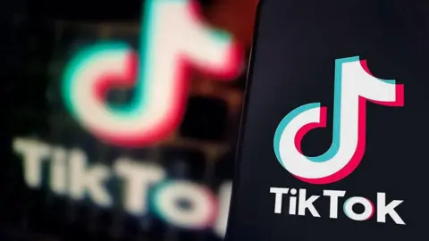 TikTok's logo displayed on a smartphone screen, with the app's logo blurred in the background behind it.