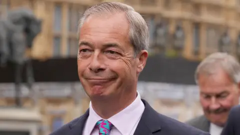 Reform UK leader Nigel Farage smiles as he arrives at the House of Commons in Westminster wearing a suit with a colourful tie.