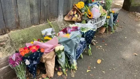 Bunches of flowers sit in a row on a street corner. A road sign reads Stanton Avenue.