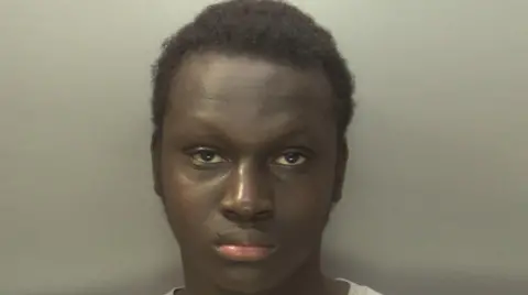 Oumar is staring at the camera and has short, dark hair and a grey top on.