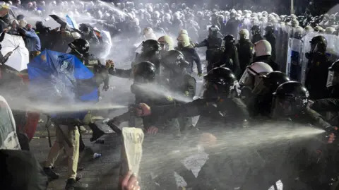 Getty Images Riot police use pepper spray on protesters, who cover themselves with umbrellas and placards, in Istanbul