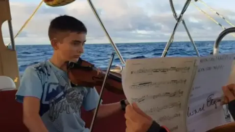 Family handout A young boy plays the violin on a boat. 
