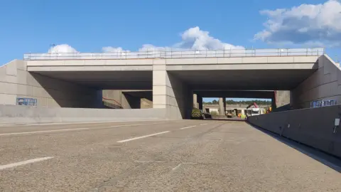 A brand new concrete bridge stretching over the closed M25 motorway.