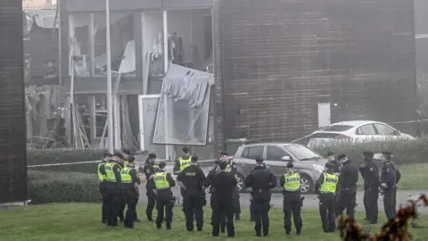 ANDERS WIKLUND/TT NEWS AGENCY/AFP Polisi berdiri di depan sebuah bangunan yang rusak setelah ledakan dahsyat terjadi pada dini hari tanggal 28 September 2023 di kawasan perumahan di Storvreta di luar Uppsala, Swedia. 