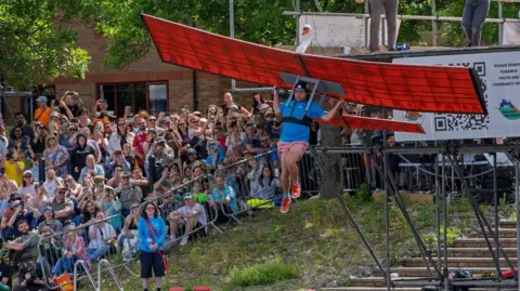 Big crowd watching a man attached to a wings shaped like a swan plunging into the water.