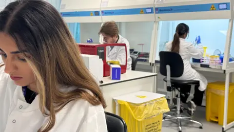 Three people wearing white coats work in a lab.