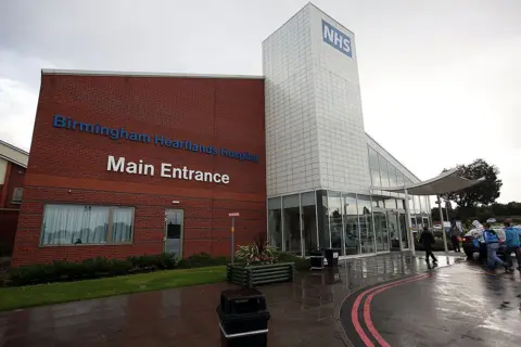 Getty A red brick building with a chrome and glass tower in the centre. A sign says "Birmingham Heartlands Hospital" in blue on the redbrick wall. 