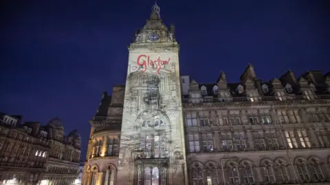 PA Media A large Victorian era hotel building in Glasgow, with a light showing shining over it. GLASGOW is spelled out in red.